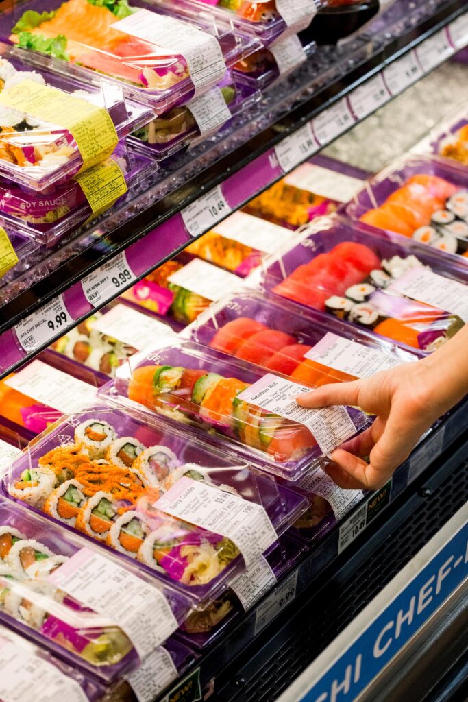 A hand selecting a pre-packaged sushi from the display at a grocery store